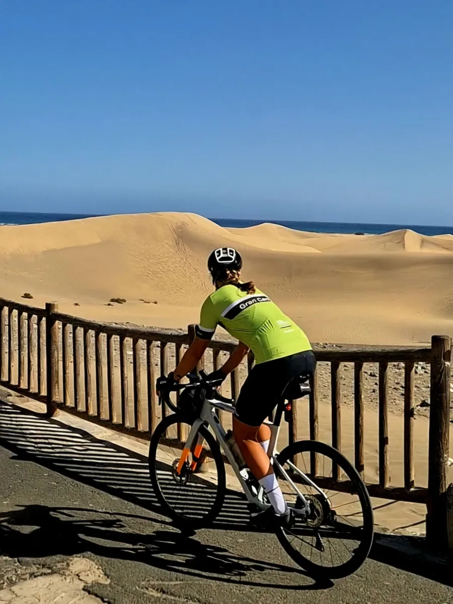 Emma riding her bike along a wooden fence by sand dunes and the sea