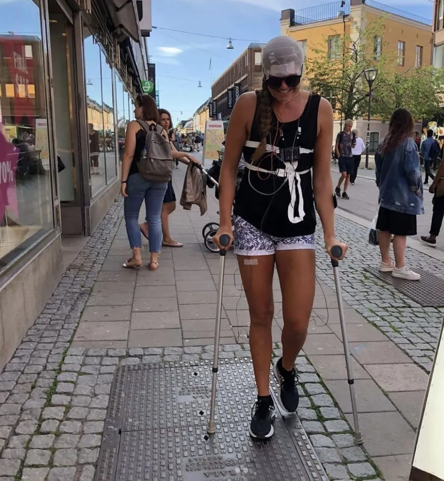 Emma på kryckor på en gata, kopplad till en smärtmätningssele efter en operation